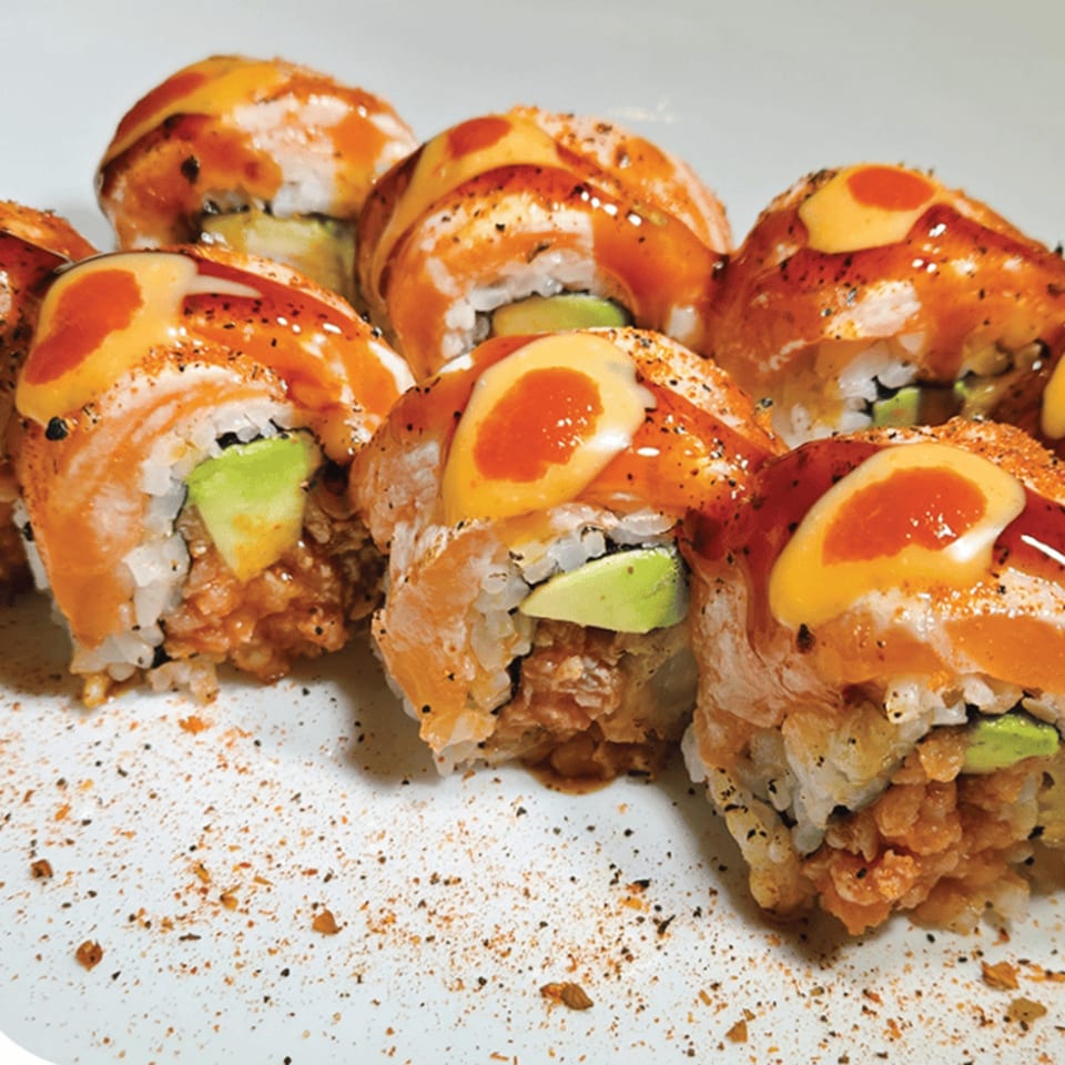 Close-up of Koji Ramen's sushi rolls, topped with salmon, avocado, and drizzled sauces.