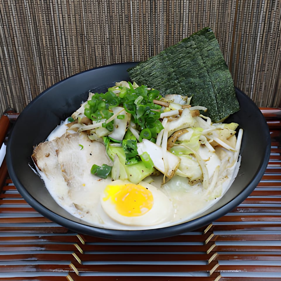 A bowl of Koji Ramen with pork, egg, green onions, and seaweed on a bamboo mat.