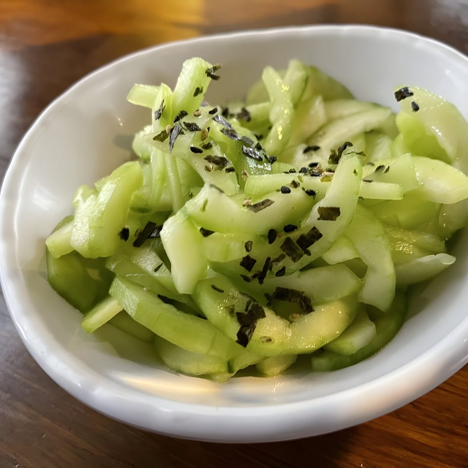 A white bowl filled with bright green sliced cucumbers, topped with dark green herbs.