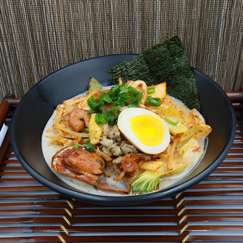 Seafood ramen with shrimp, crab, squid, egg, and seaweed in a black bowl.